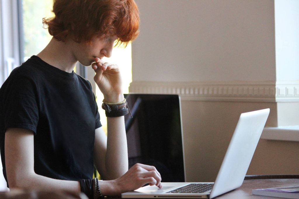 Ein junger Teenager mit rotem Haar und schwarzem T-Shirt schaut auf einen Laptop-Bildschirm 