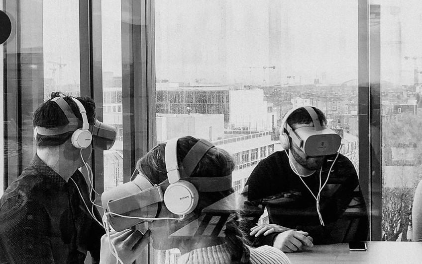 a black and white image of several people wearing VR headsets by a large window